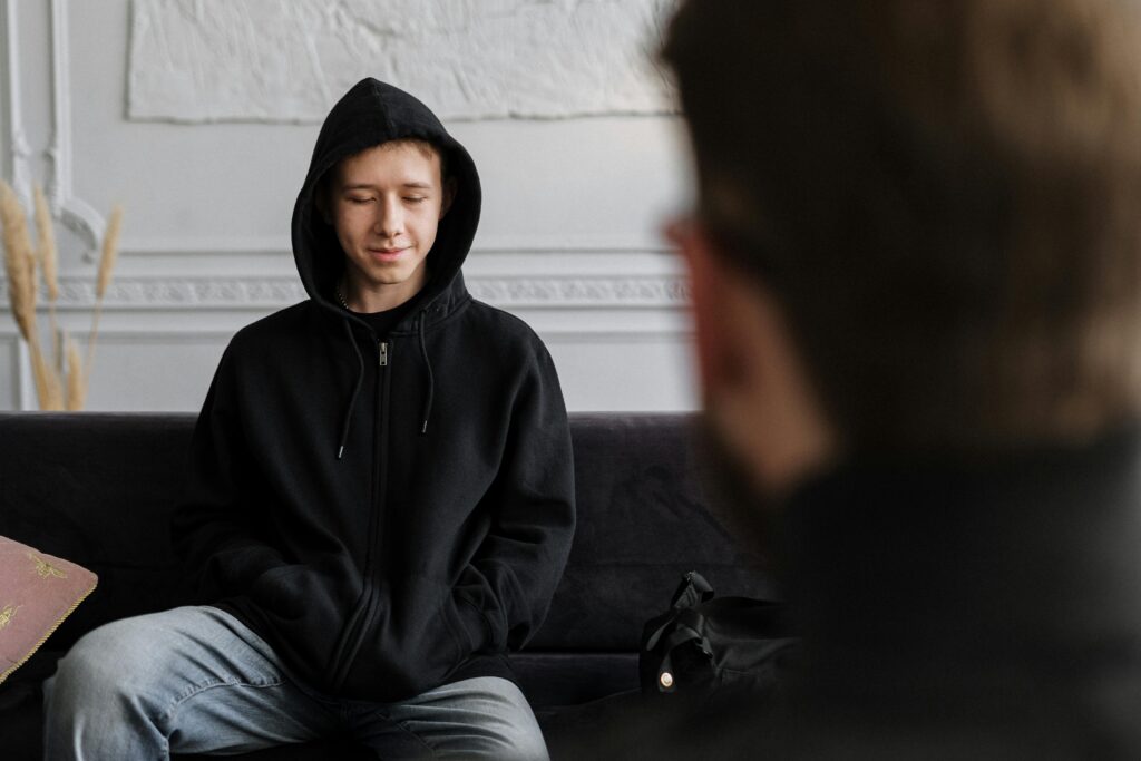 A therapist engages with a teenager wearing a hoodie during a counseling session in a cozy office.