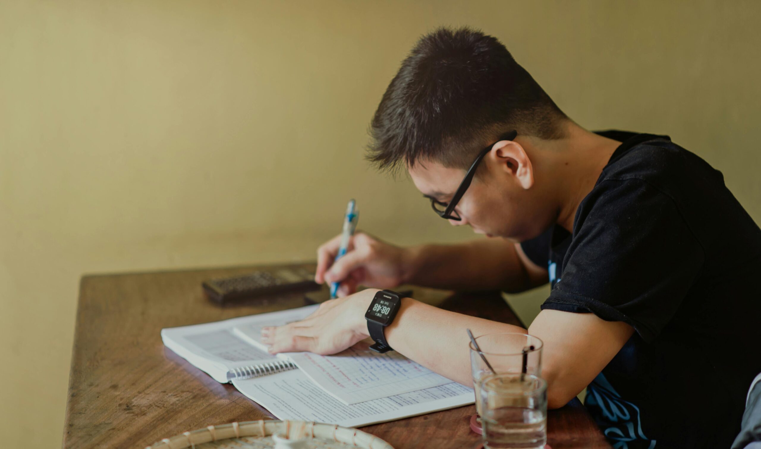 Ana Sayfa A young man concentrates on studying at his desk, taking notes indoors.